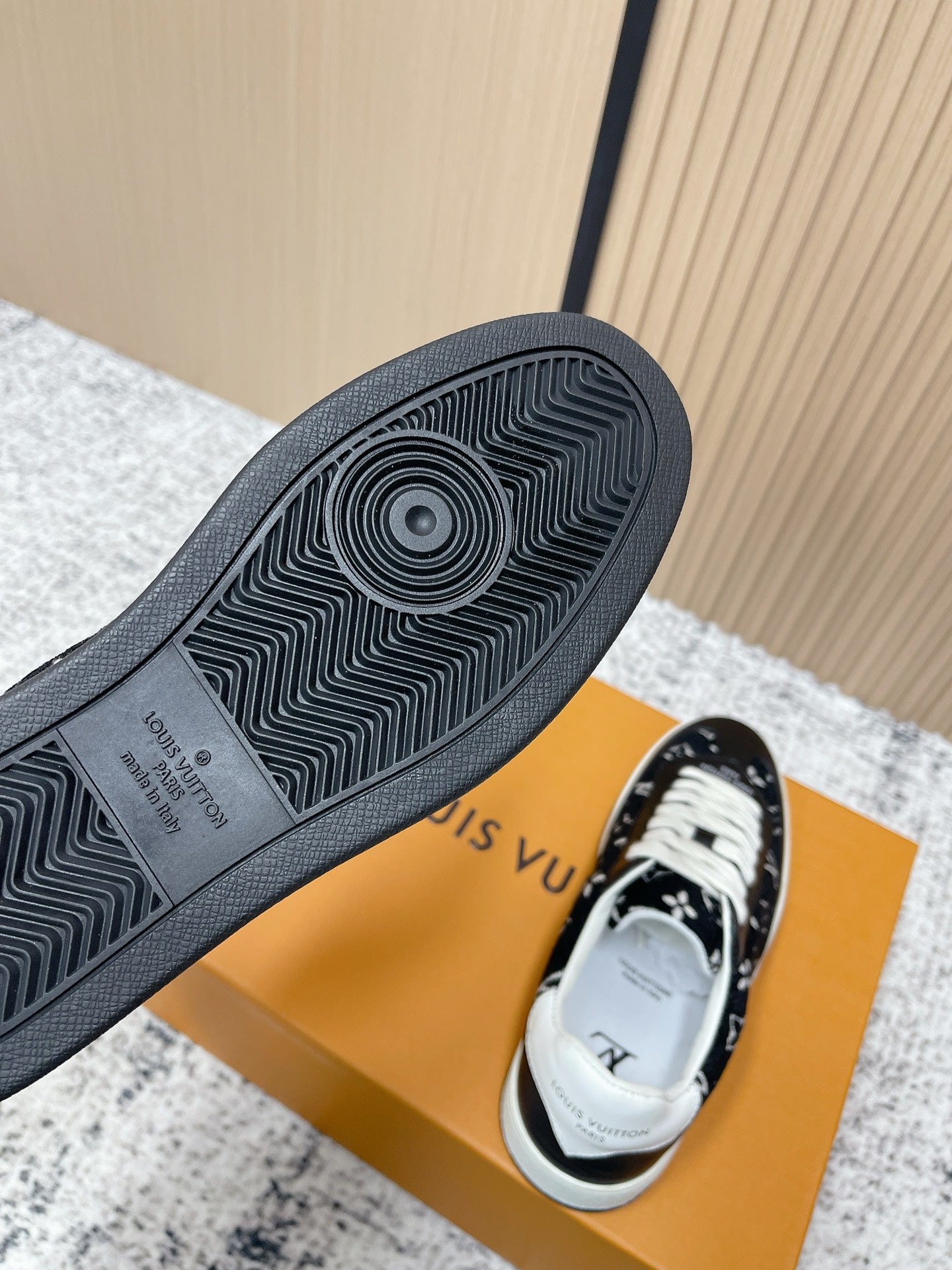 Shoe soles of black low-top sneakers with white laces, viewed from the bottom on box.