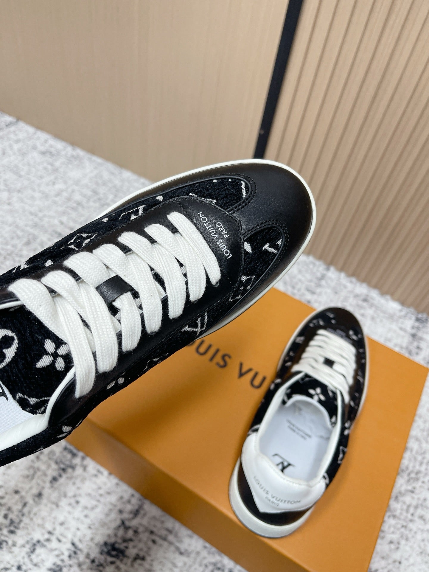 Black low-top sneakers with white laces and monogram-style print, toe-and-heel angle.