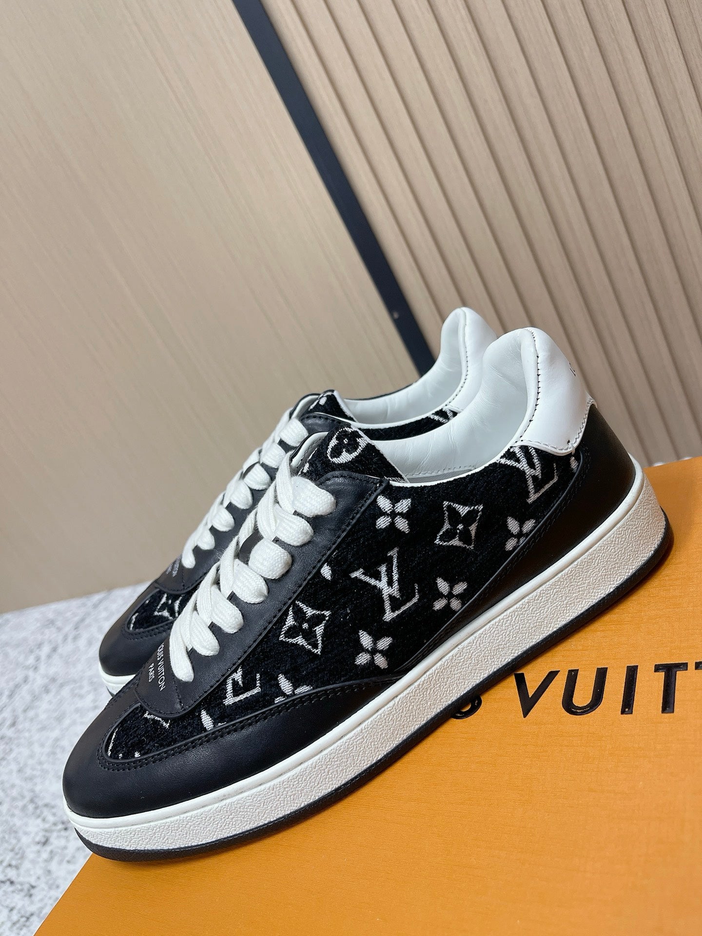 Black low-top sneakers with white laces and monogram-style print, angled front view.