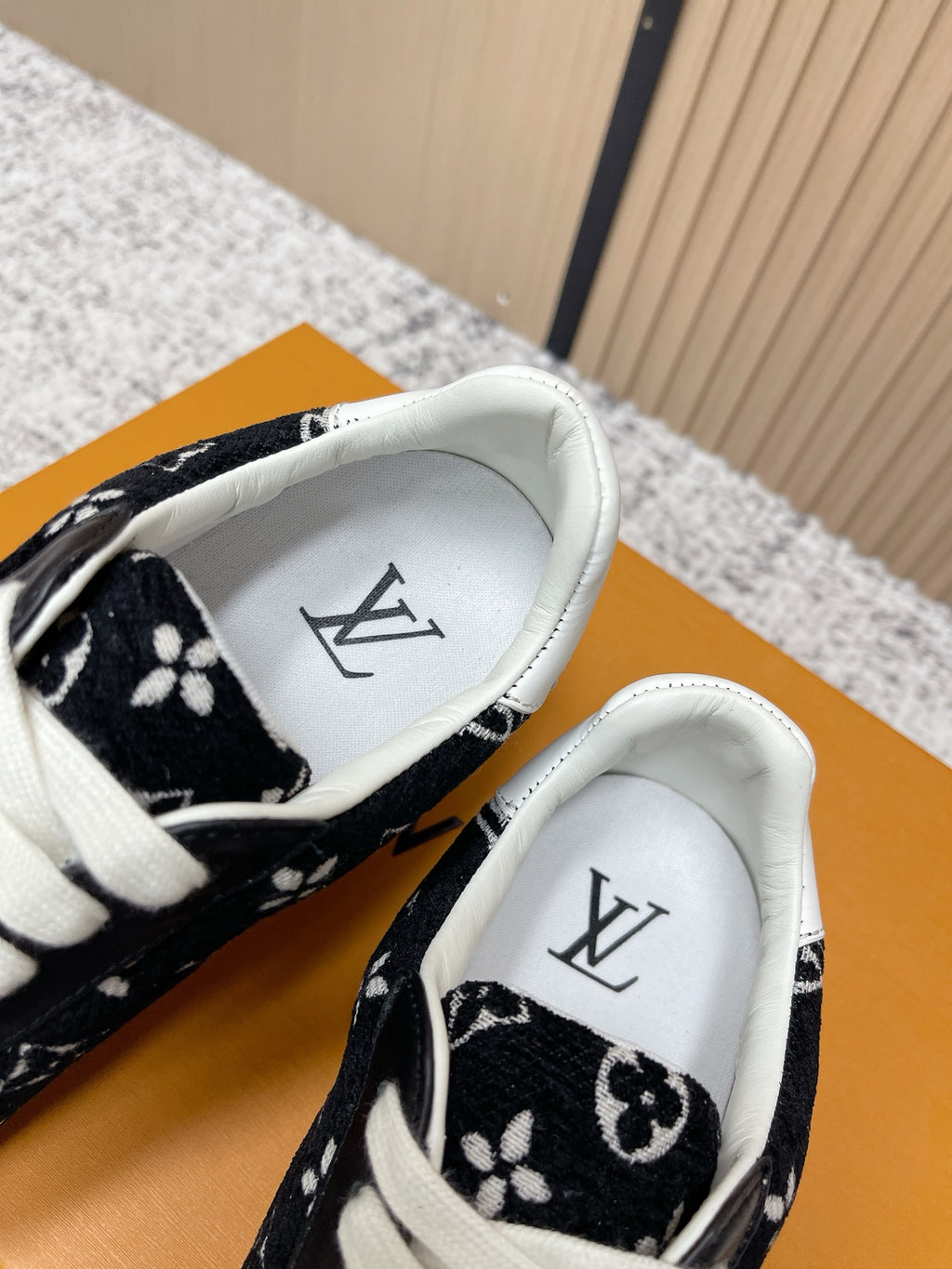 Black low-top sneakers with white interior lining and monogram pattern, close-up.