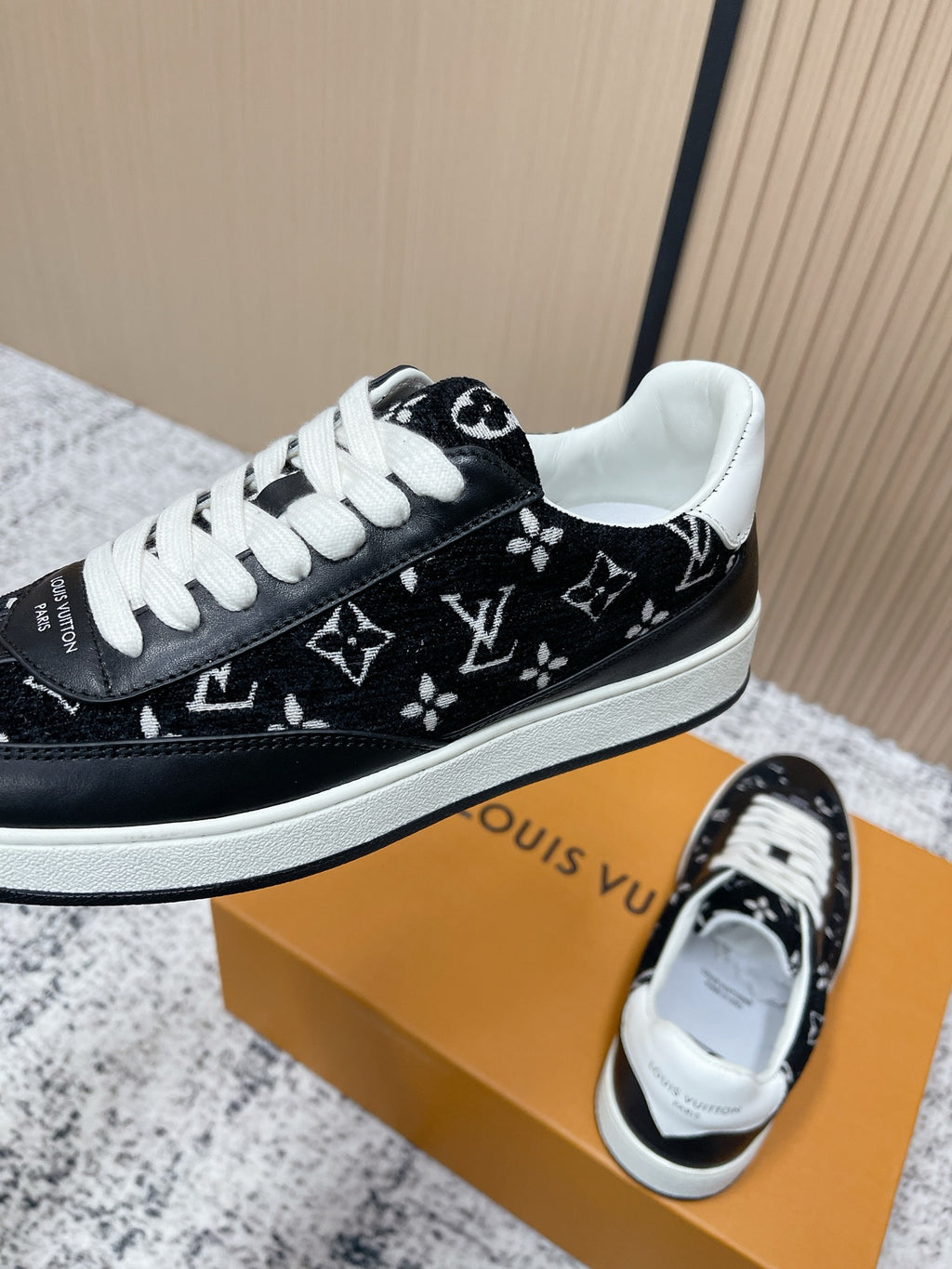 Black low-top sneakers with white laces and monogram-style print, side view on box.