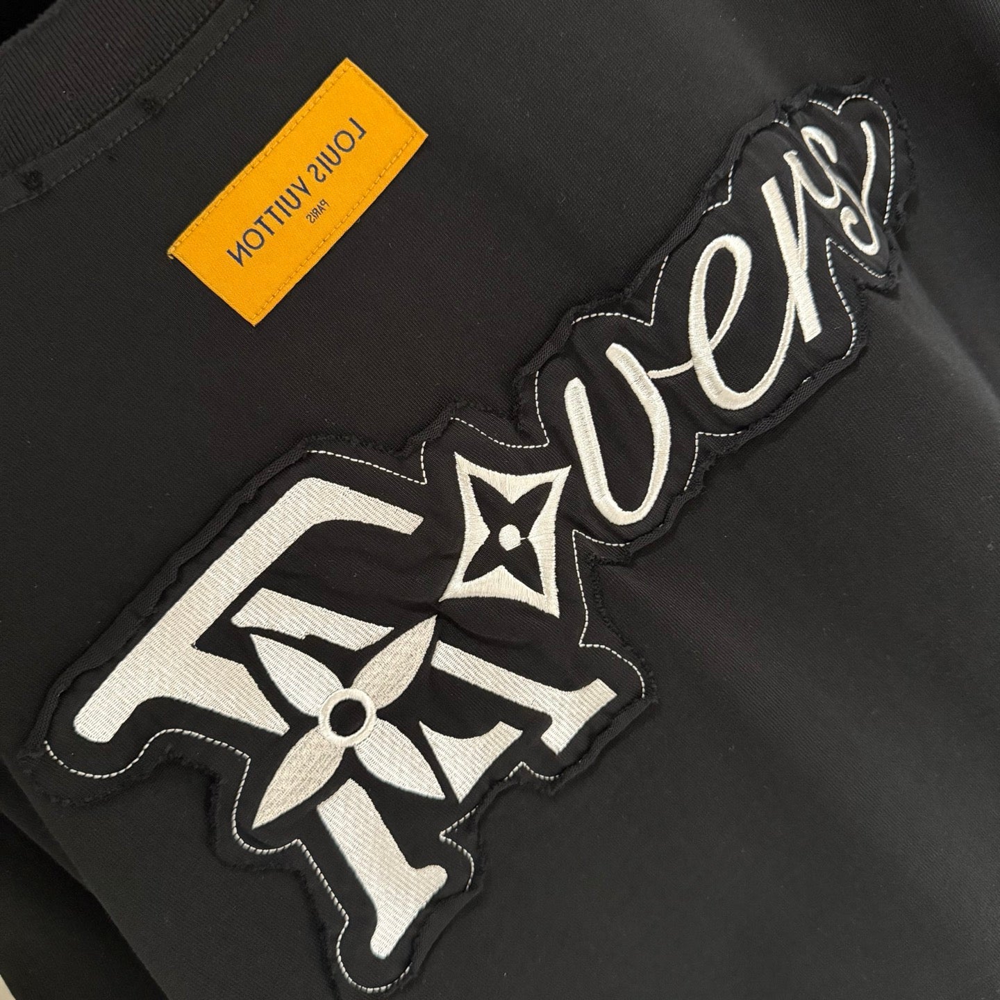 Black T-shirt detail with embroidered 'Lovers' logo graphic and star motif