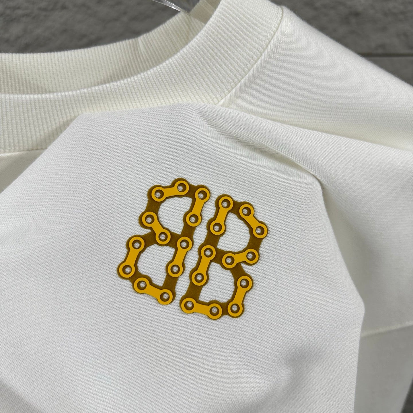 Close-up of white sweatshirt with gold Balenciaga monogram patch