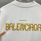 White crew-neck sweatshirt with gold Balenciaga text graphic across the front