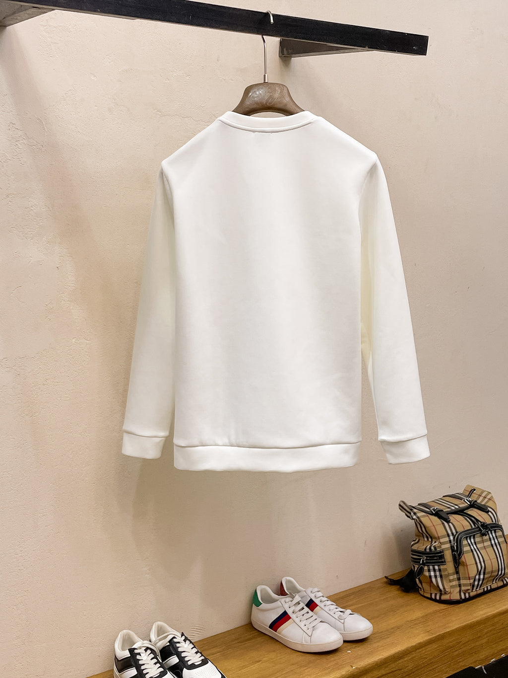 Back view of white crewneck sweatshirt hanging on a rack.