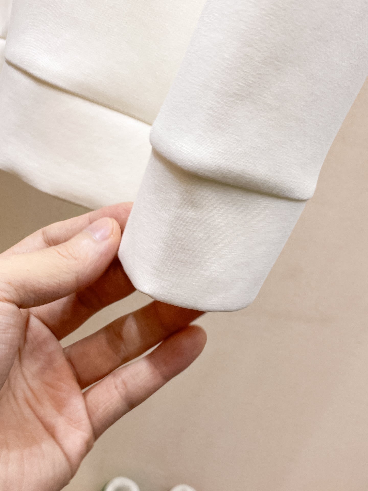 White crewneck sweatshirt cuff with hand holding sleeve hem seam.
