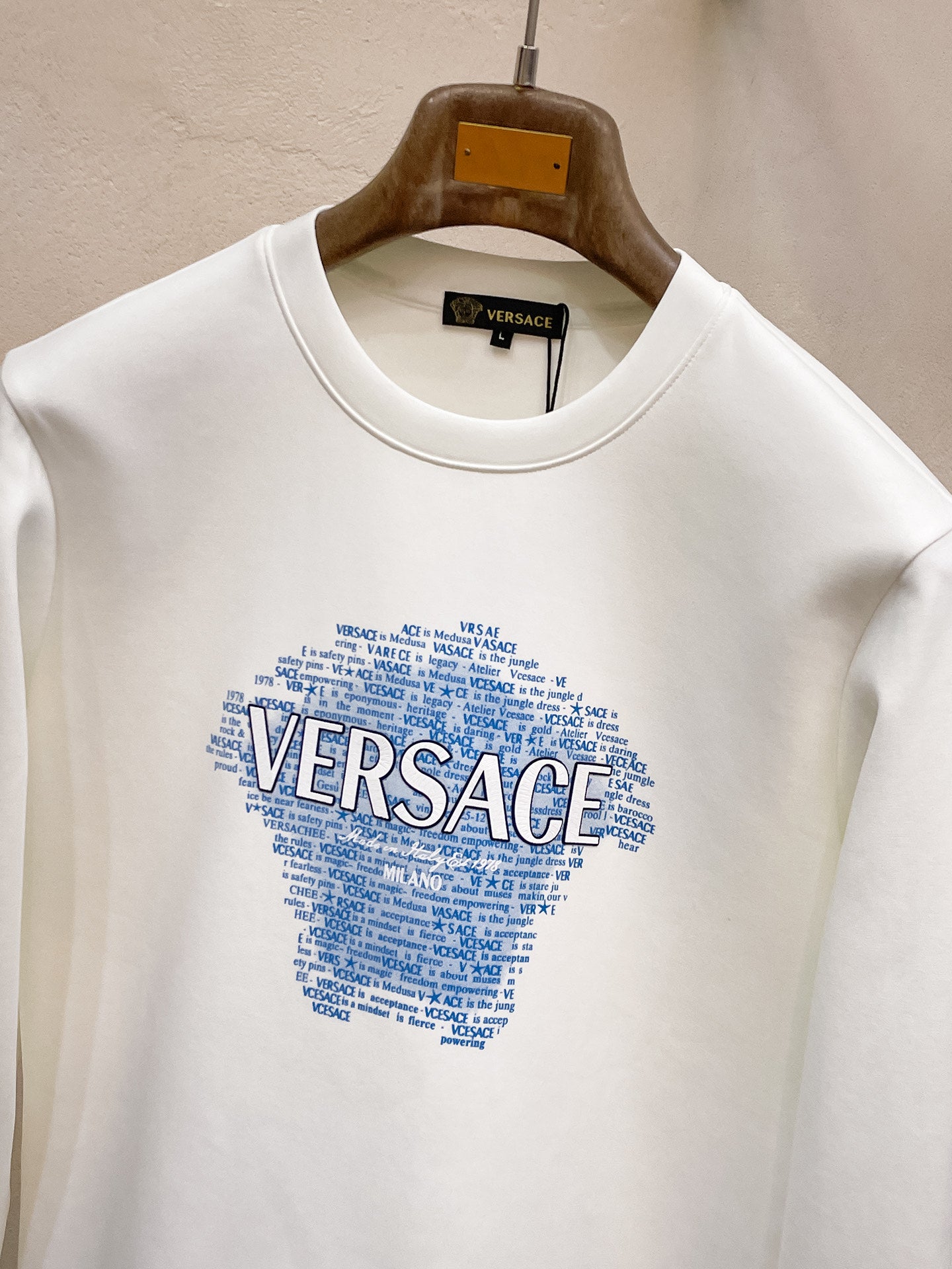 White crewneck sweatshirt with Versace logo graphic and small text detail at neckline.