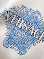 White crewneck sweatshirt with large blue Versace word graphic and dense text print.