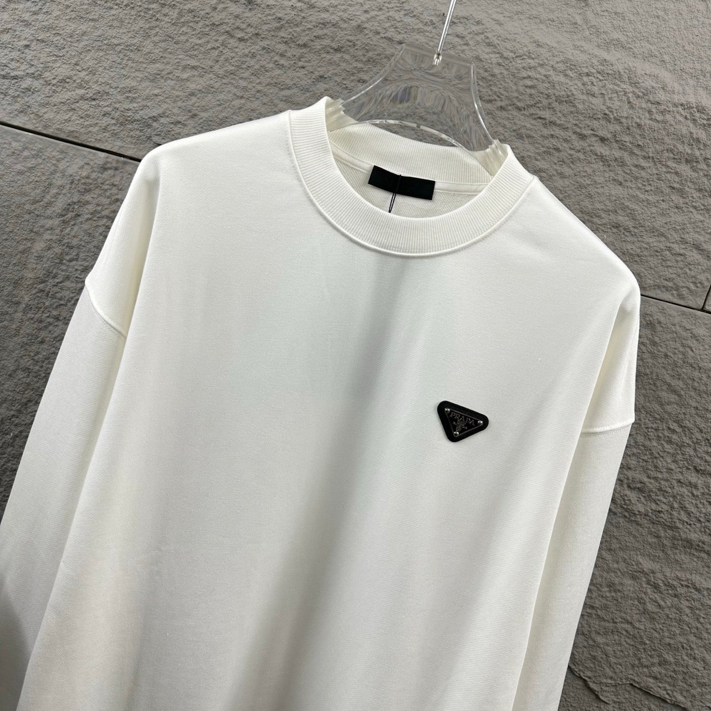 Off-white Prada sweatshirt close-up, crew neck and black triangular logo patch.