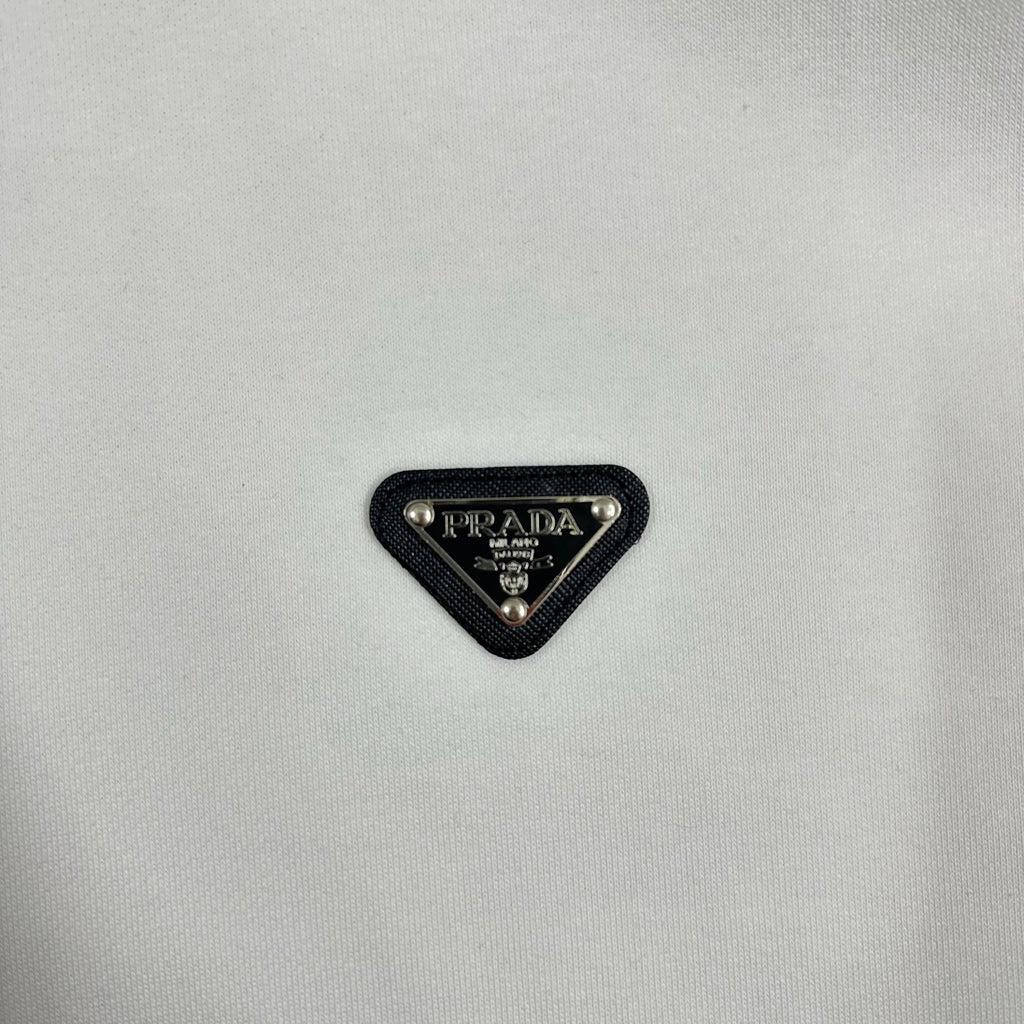 Black triangular Prada logo patch on off-white sweatshirt fabric.