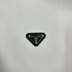 Black triangular Prada logo patch on off-white sweatshirt fabric.