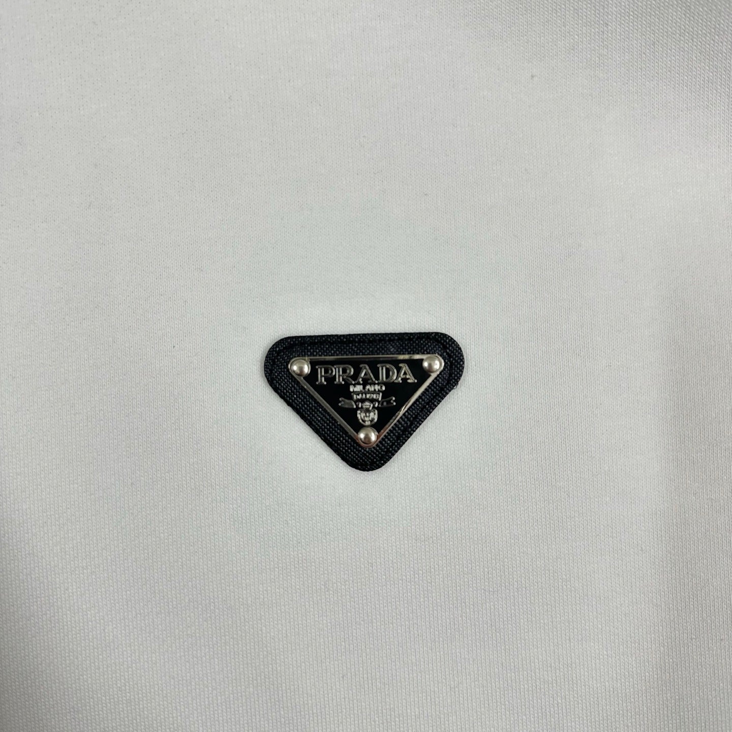 Black triangular Prada logo patch on off-white sweatshirt fabric.