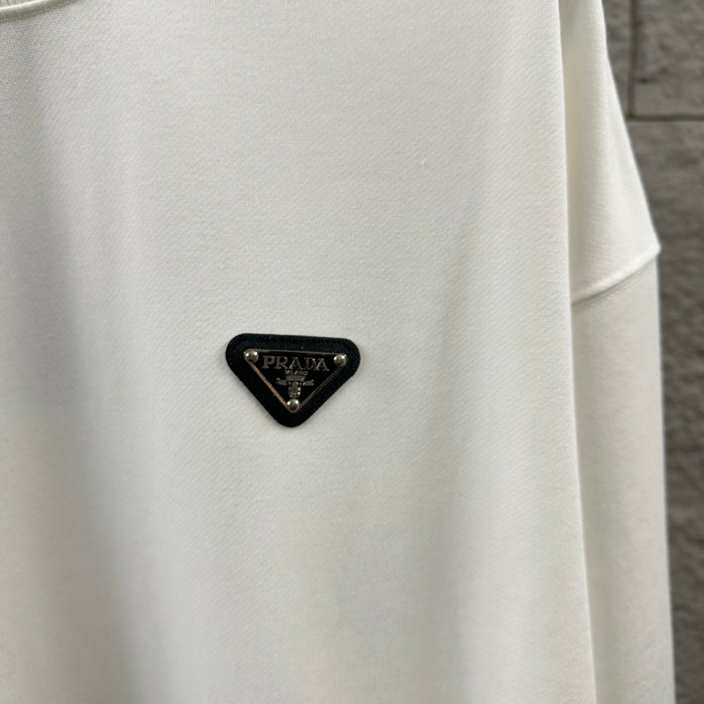 Off-white Prada sweatshirt with black triangular logo patch near the chest.