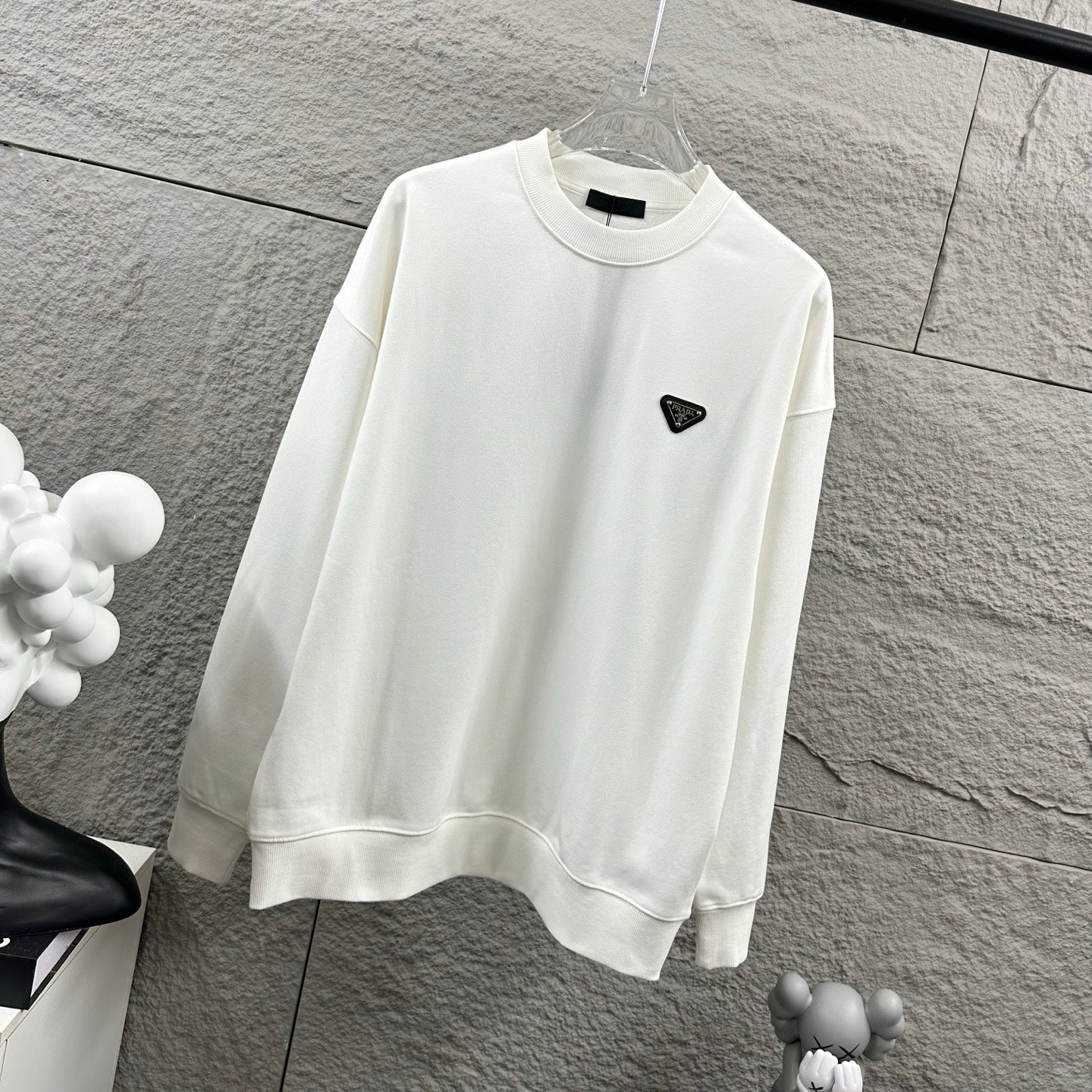 Off-white Prada sweatshirt with ribbed cuffs and black triangular logo patch.
