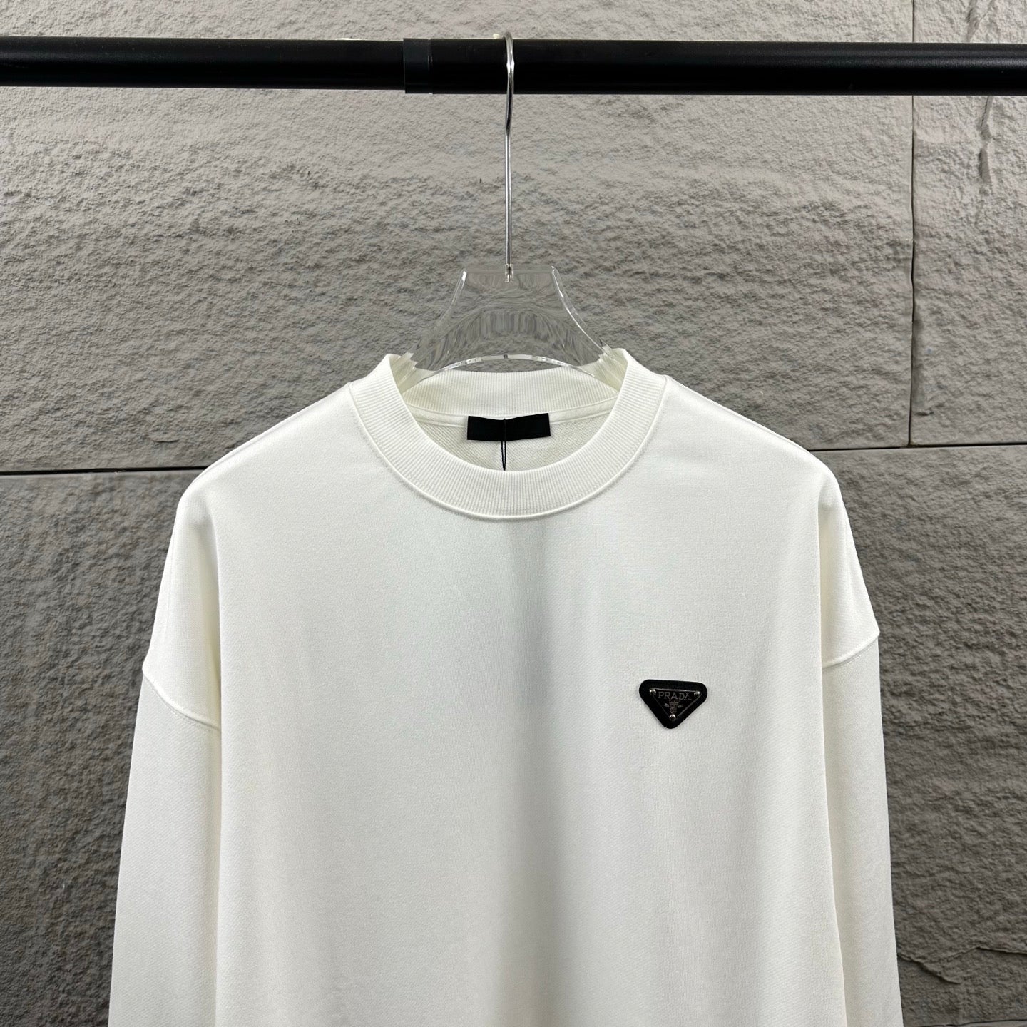 Off-white Prada crewneck sweatshirt with black triangular logo patch on chest.