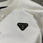 Off-white sweatshirt chest patch: black triangular Prada logo with metallic text.