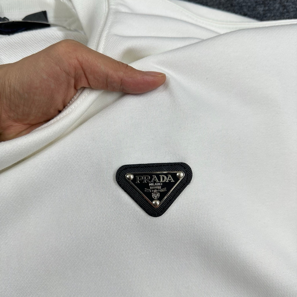 Off-white Prada sweatshirt fabric with black triangular logo patch, held by hand.