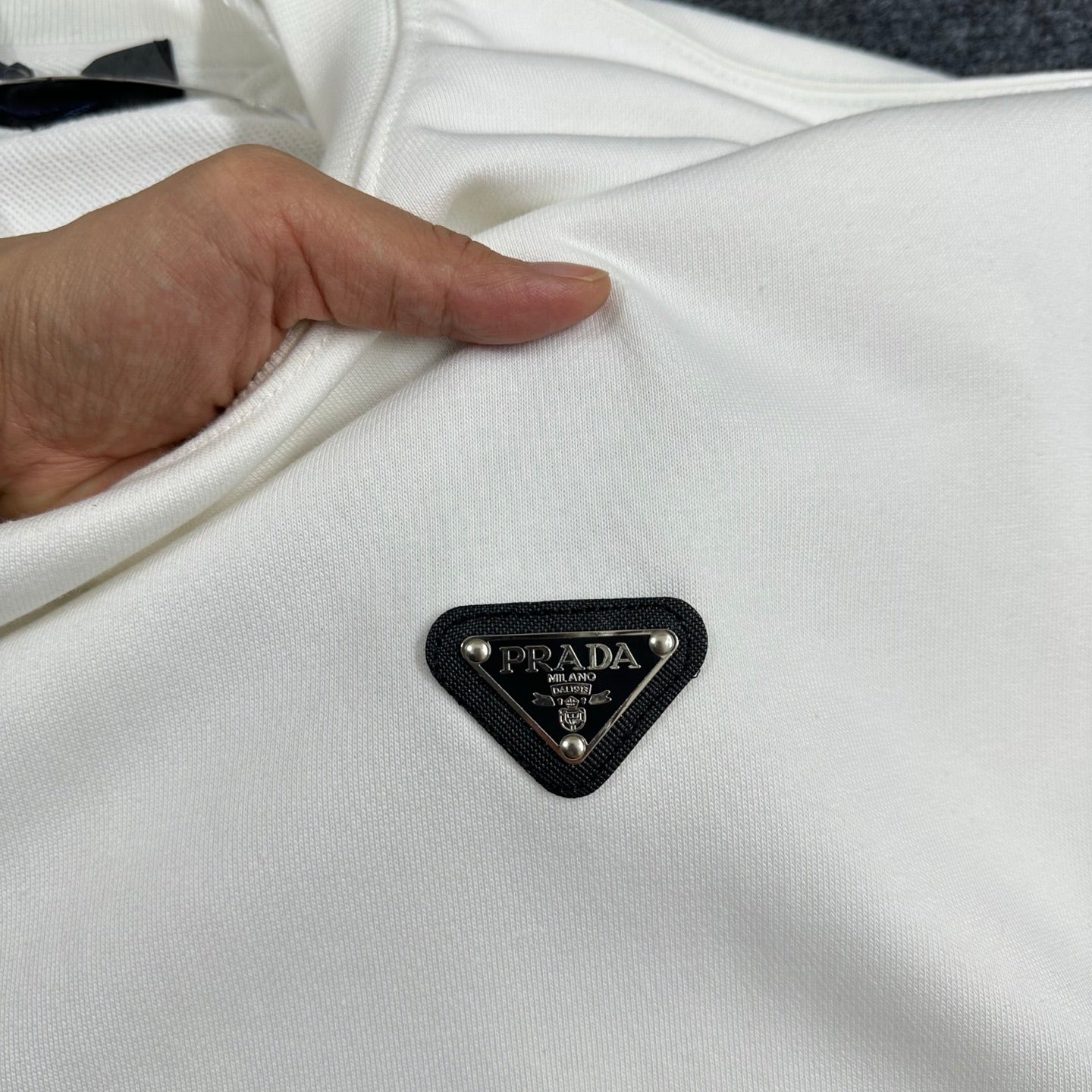 Off-white Prada sweatshirt fabric with black triangular logo patch, held by hand.