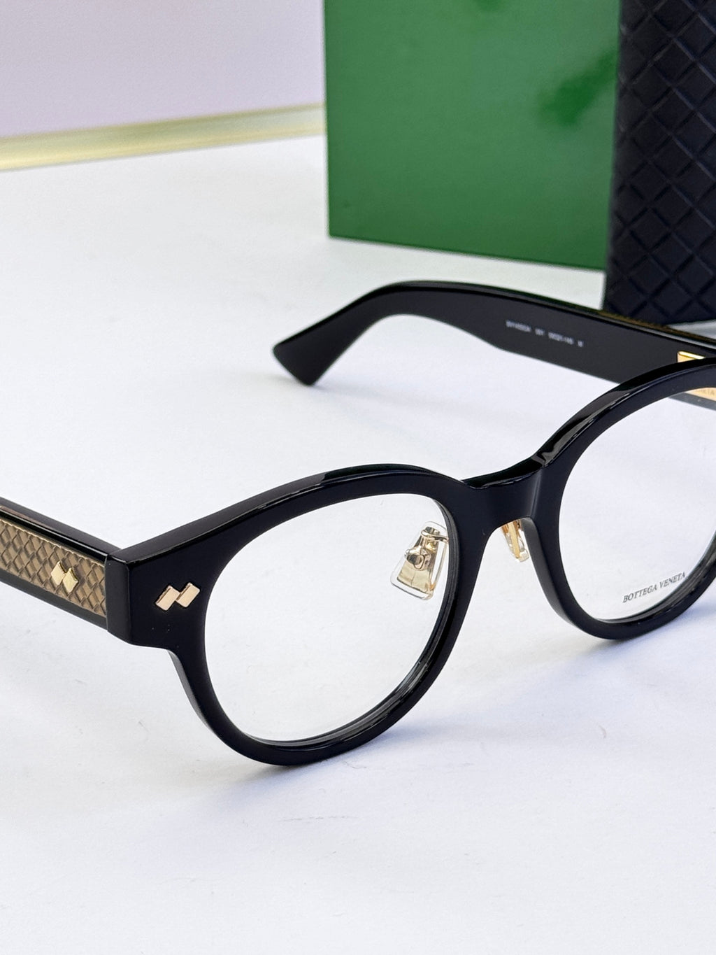 Bottega Veneta black round eyeglasses close-up with gold patterned temple trim