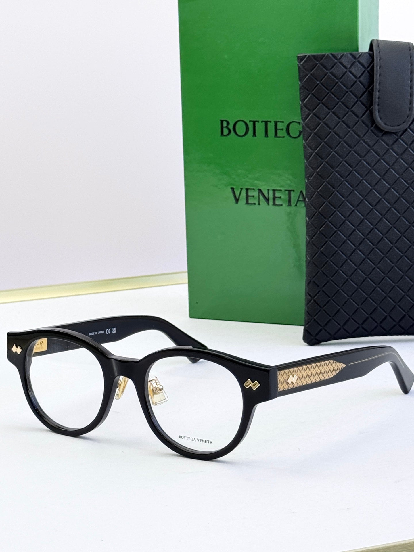 Bottega Veneta black round eyeglasses with gold patterned temples and metal hinges
