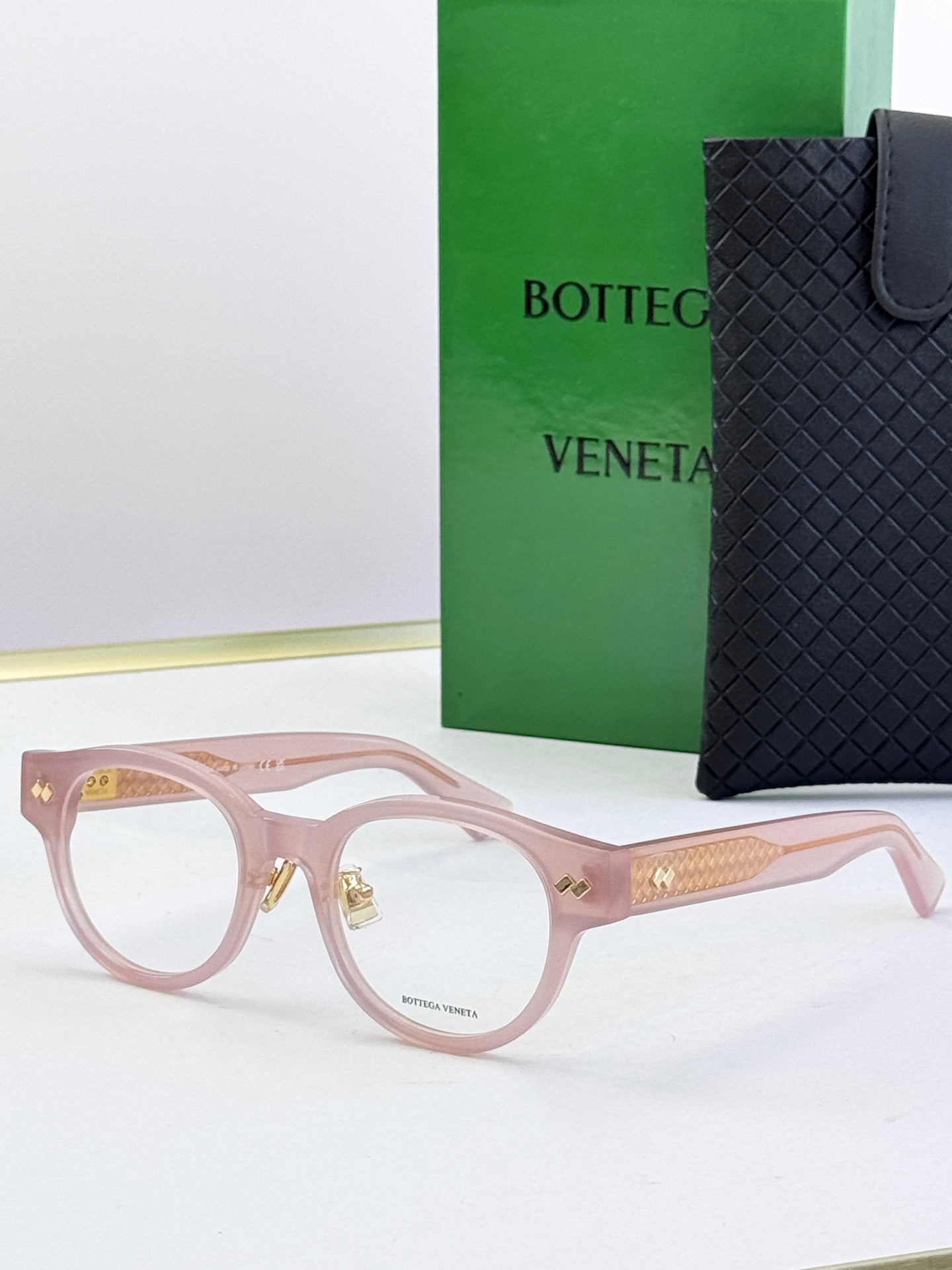 Bottega Veneta pink round eyeglasses with gold patterned temples and metal hinges