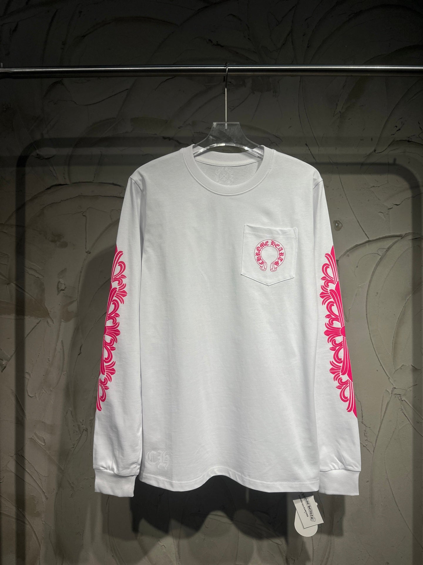 White long-sleeve T-shirt with red-pink pocket logo and sleeve scroll print.