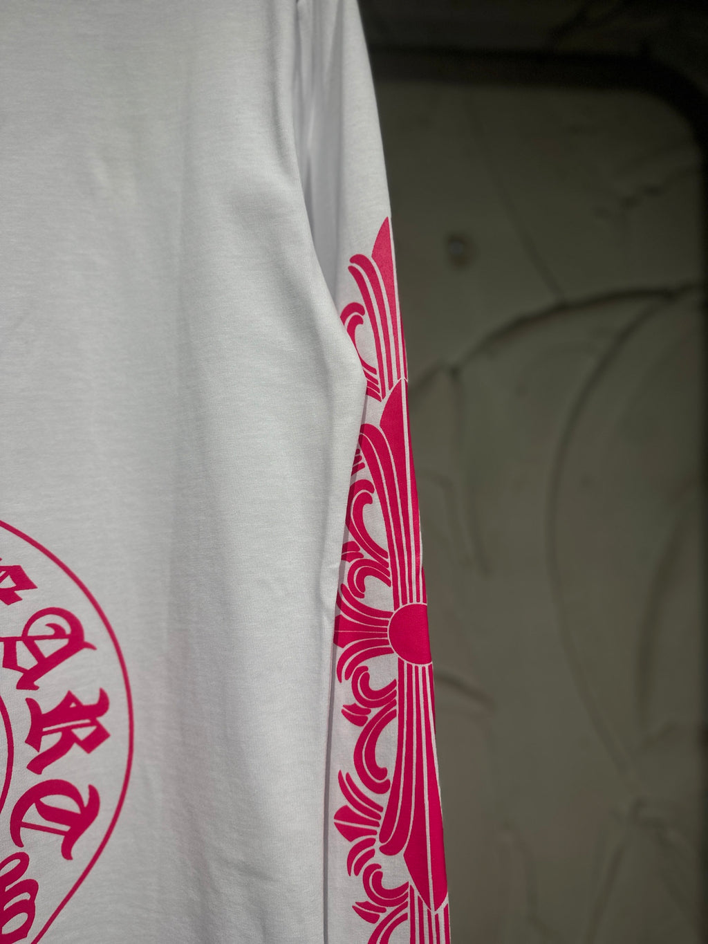 White long-sleeve T-shirt with red-pink sleeve scroll graphic near cuff.