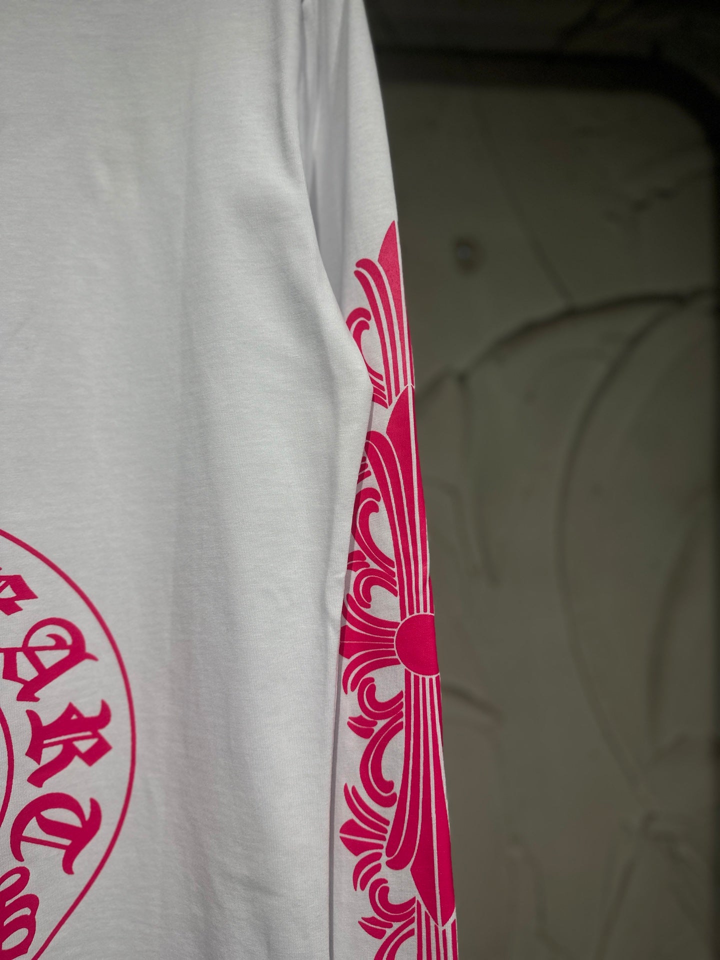 White long-sleeve T-shirt with red-pink sleeve scroll graphic near cuff.