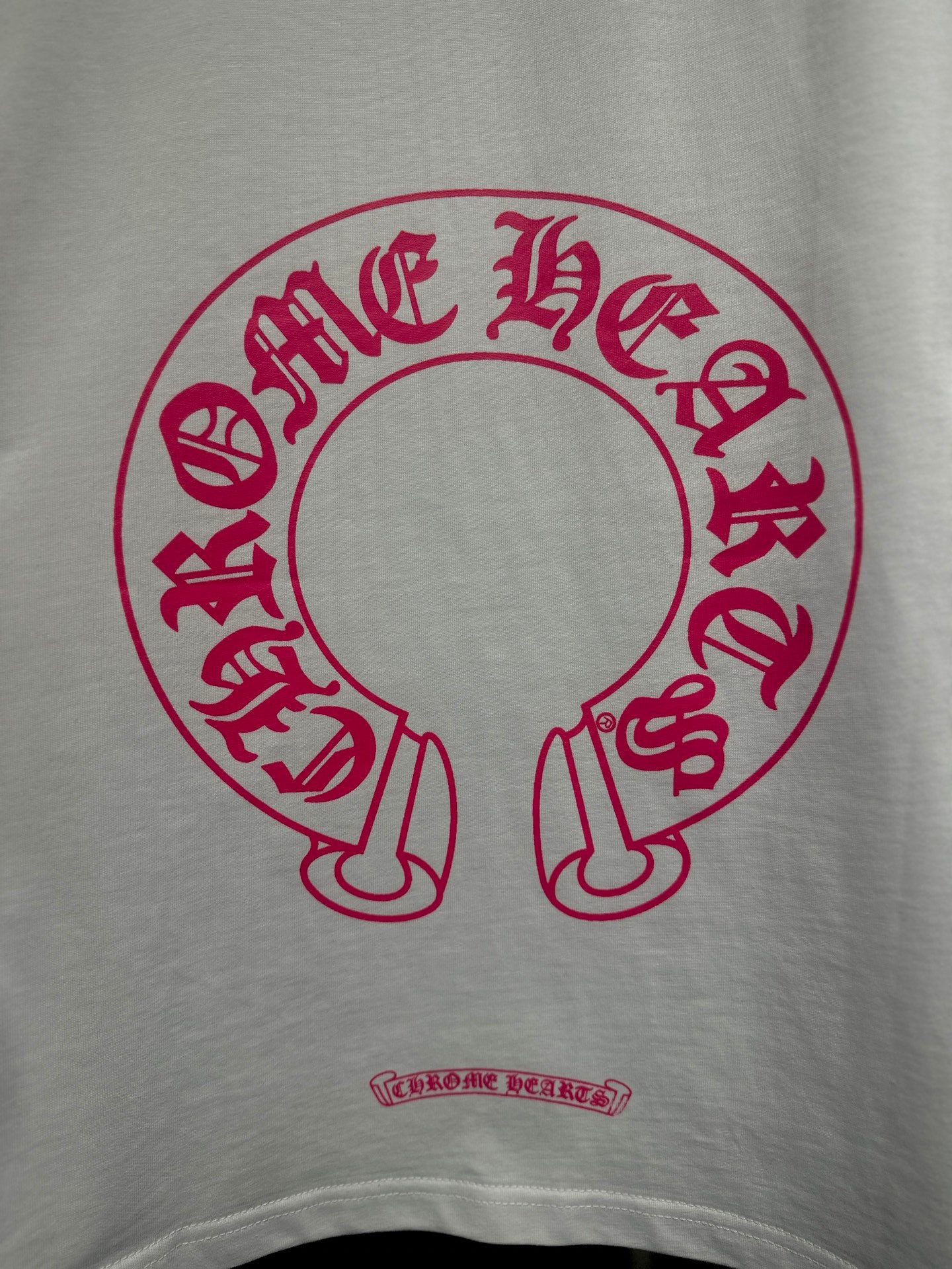 White long-sleeve T-shirt with red-pink circular logo print and small text below.