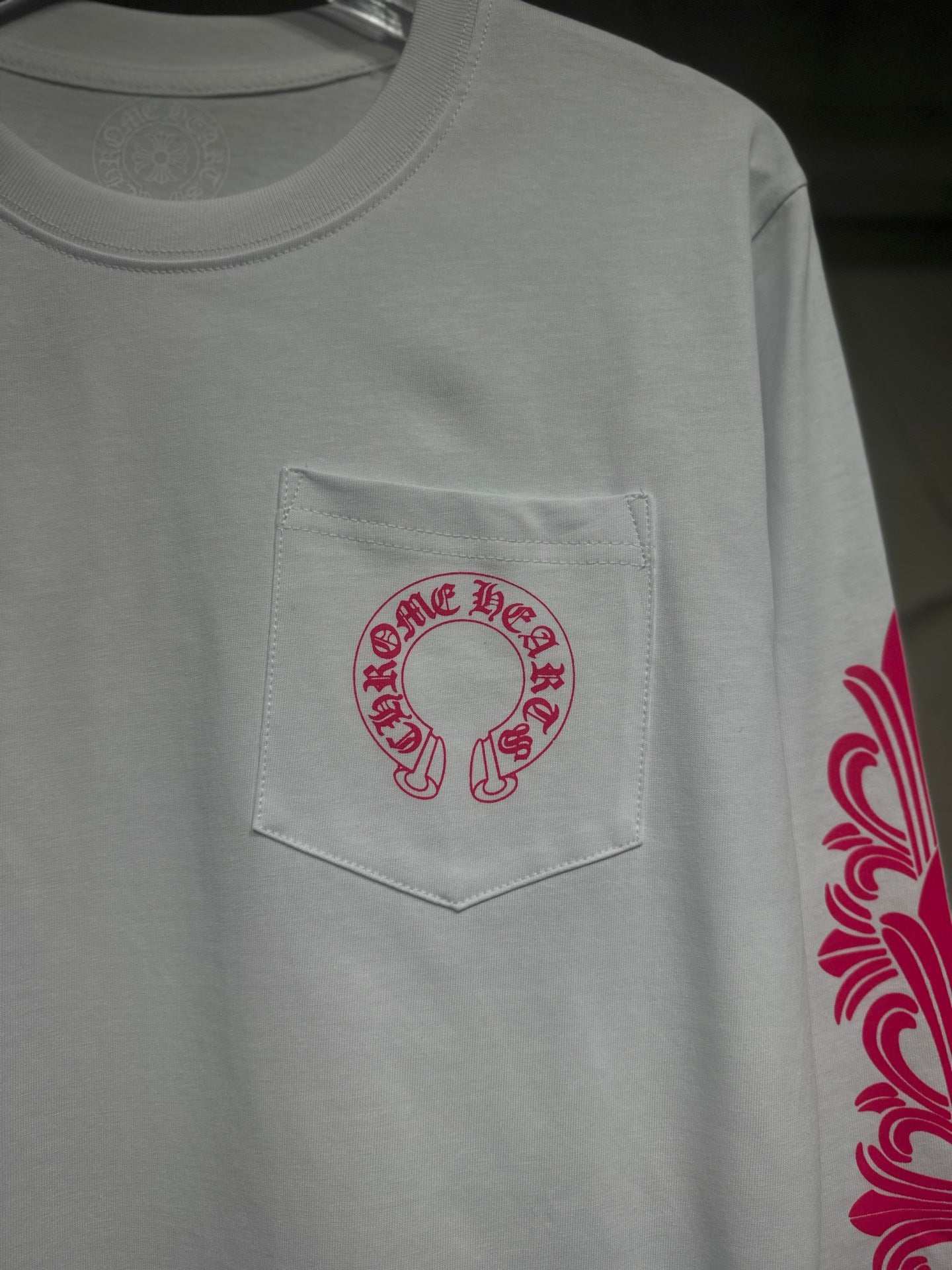 White long-sleeve T-shirt with red-pink logo patch on chest pocket.