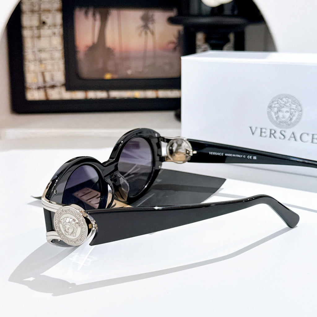 Versace sunglasses with dark lenses, black frame, and gold logo medallion on the hinge