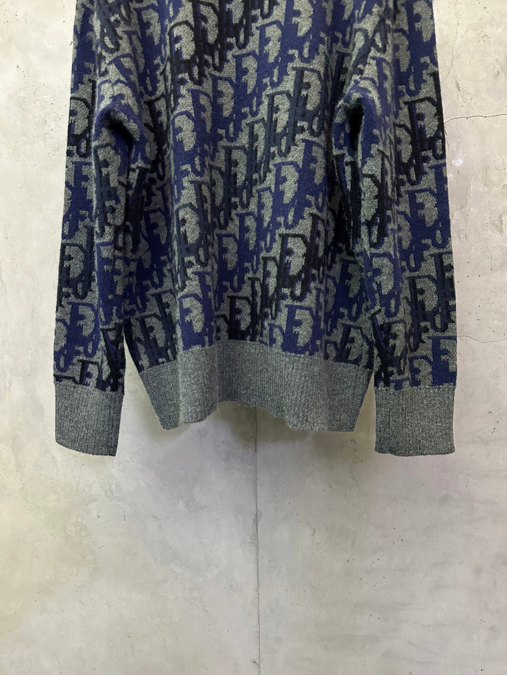 Dior knit sweater front view showing blue-and-black logo pattern and gray cuffs
