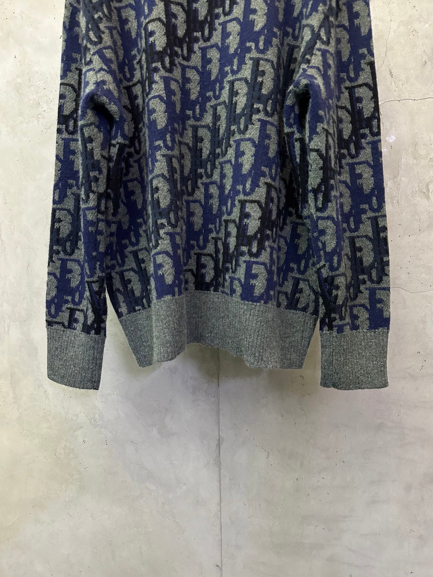 Dior knit sweater front view showing blue-and-black logo pattern and gray cuffs