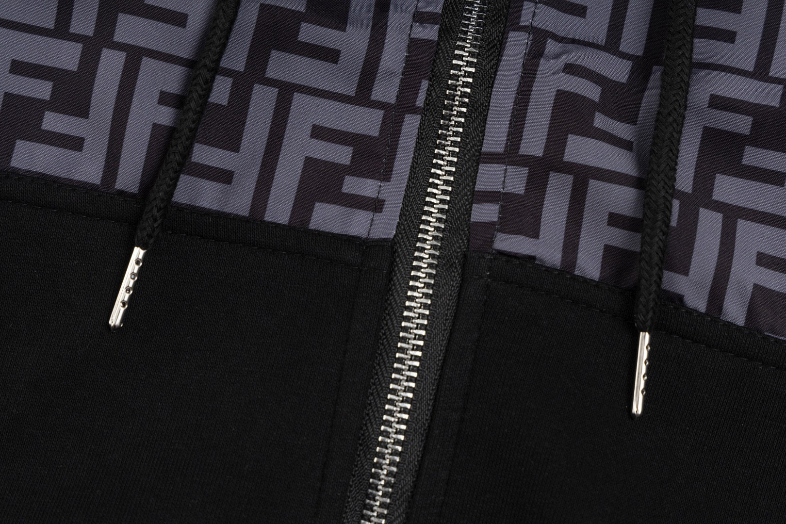 Black zip hoodie close-up with silver zipper pull and stitched seams