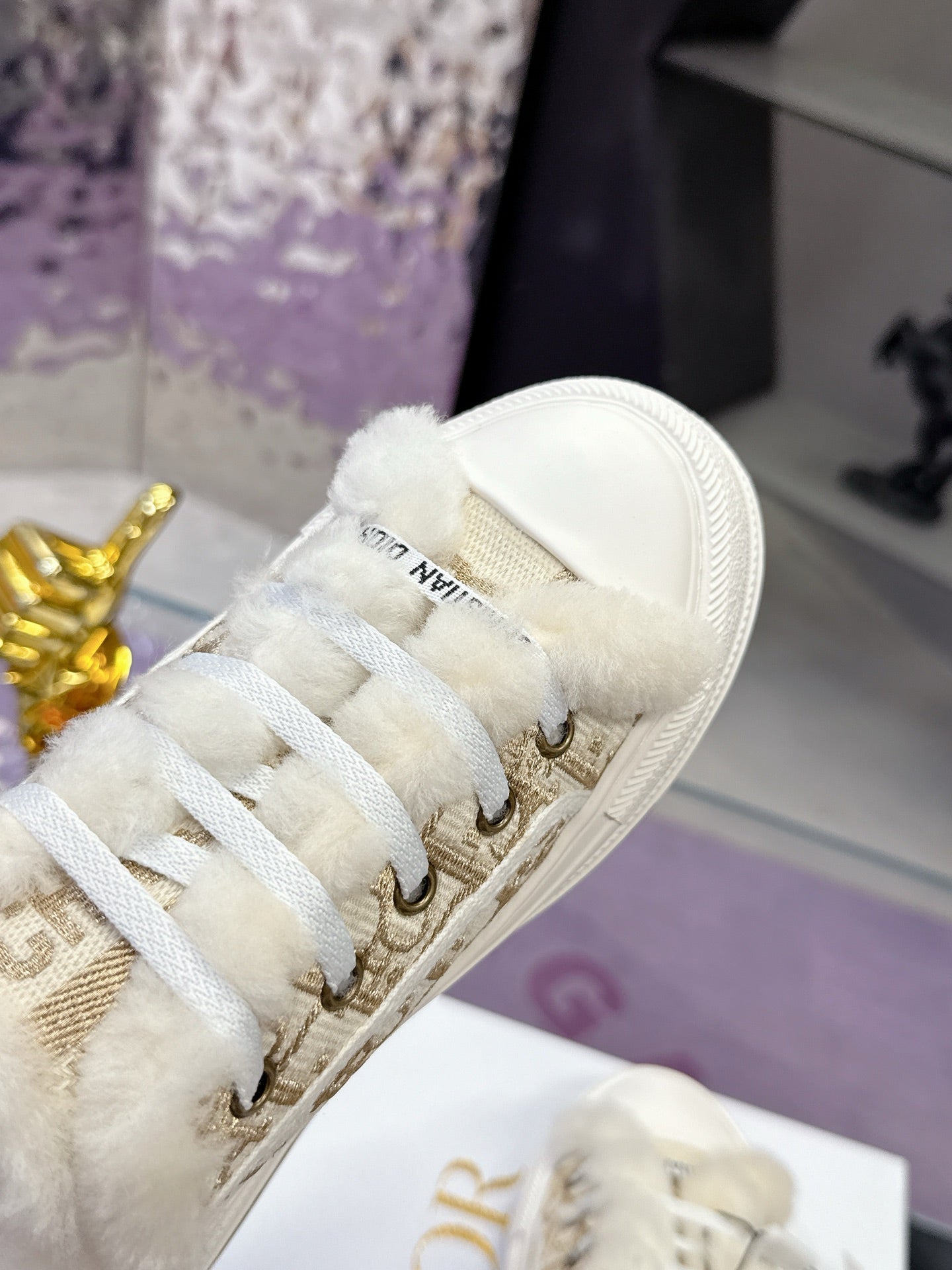 Close-up of white sneaker toe and lace panel with gold eyelets and fuzzy trim