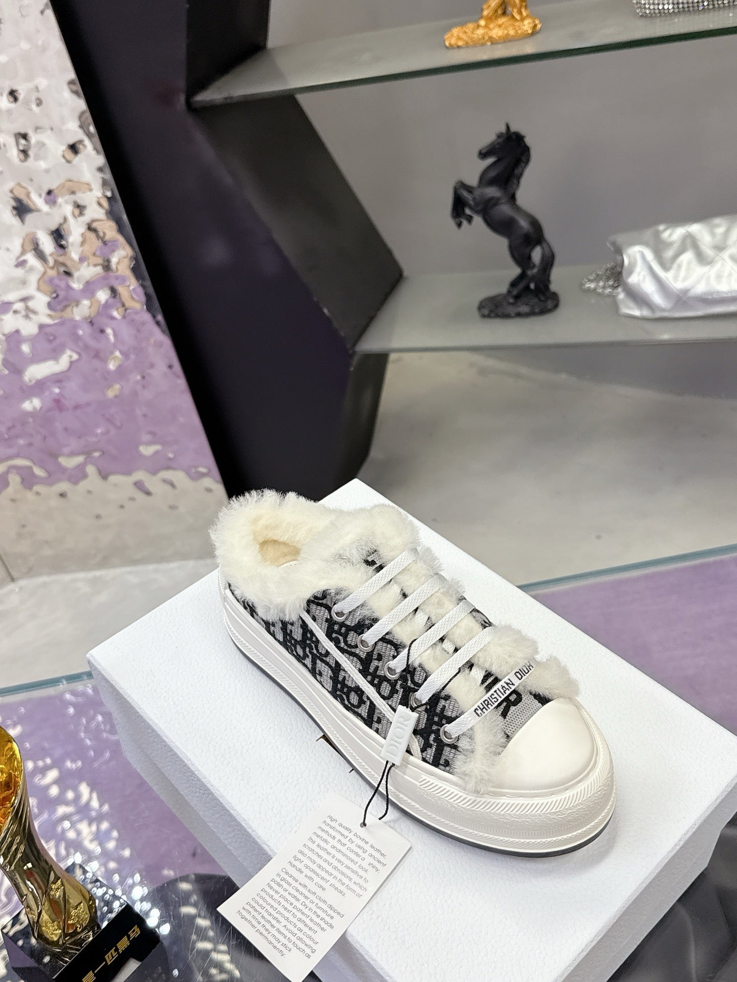 White Dior sneakers with black logo-style pattern, white laces, and fluffy collar