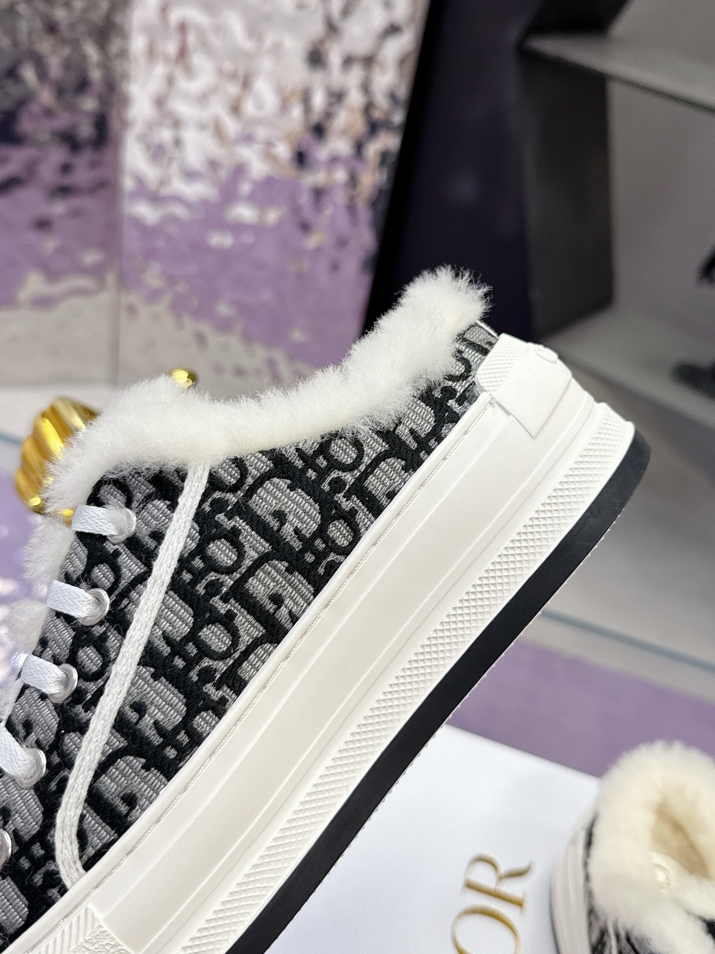 White Dior sneaker with black logo-style side, fluffy trim, and black-and-white laces