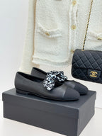 Black leather loafers with white monogram bow, round toe, and Chanel logo detail