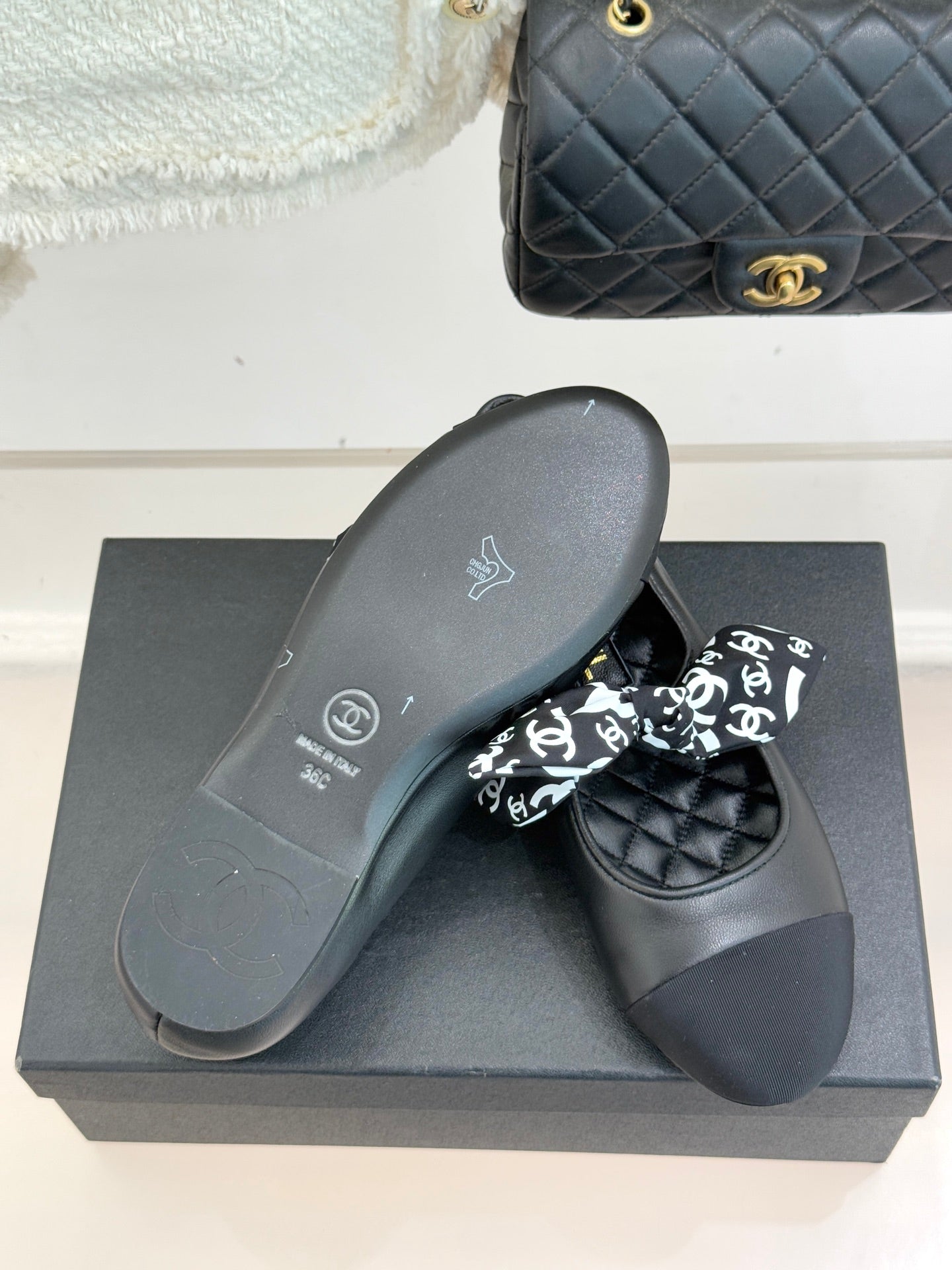 Black loafer pair with white monogram bow and flat sole on display box