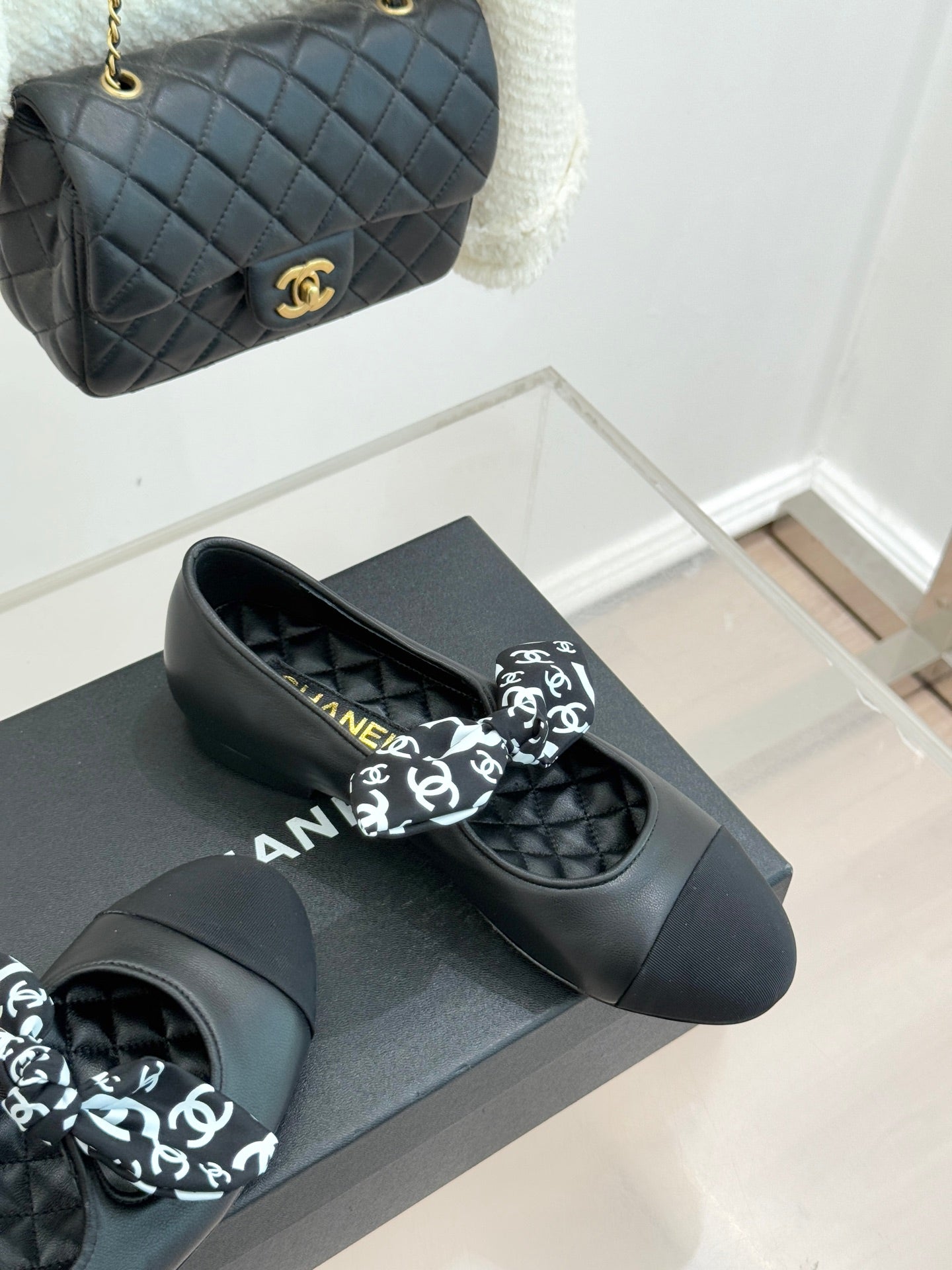 Black leather loafers with white monogram bow, side view on display box