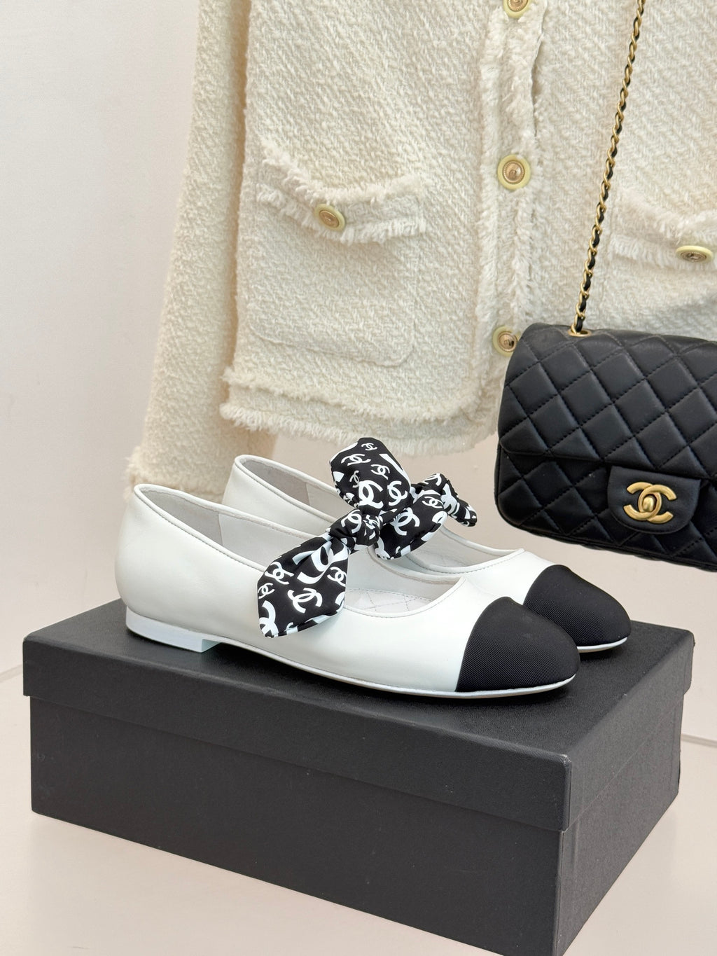 White and black Chanel ballet flats with black patterned bow and gold logo.