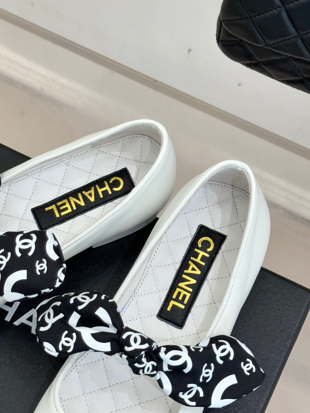 White Chanel ballet flats with CHANEL ribbon bow and black heel cap.