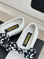 White Chanel ballet flats with CHANEL ribbon bow and black heel cap.