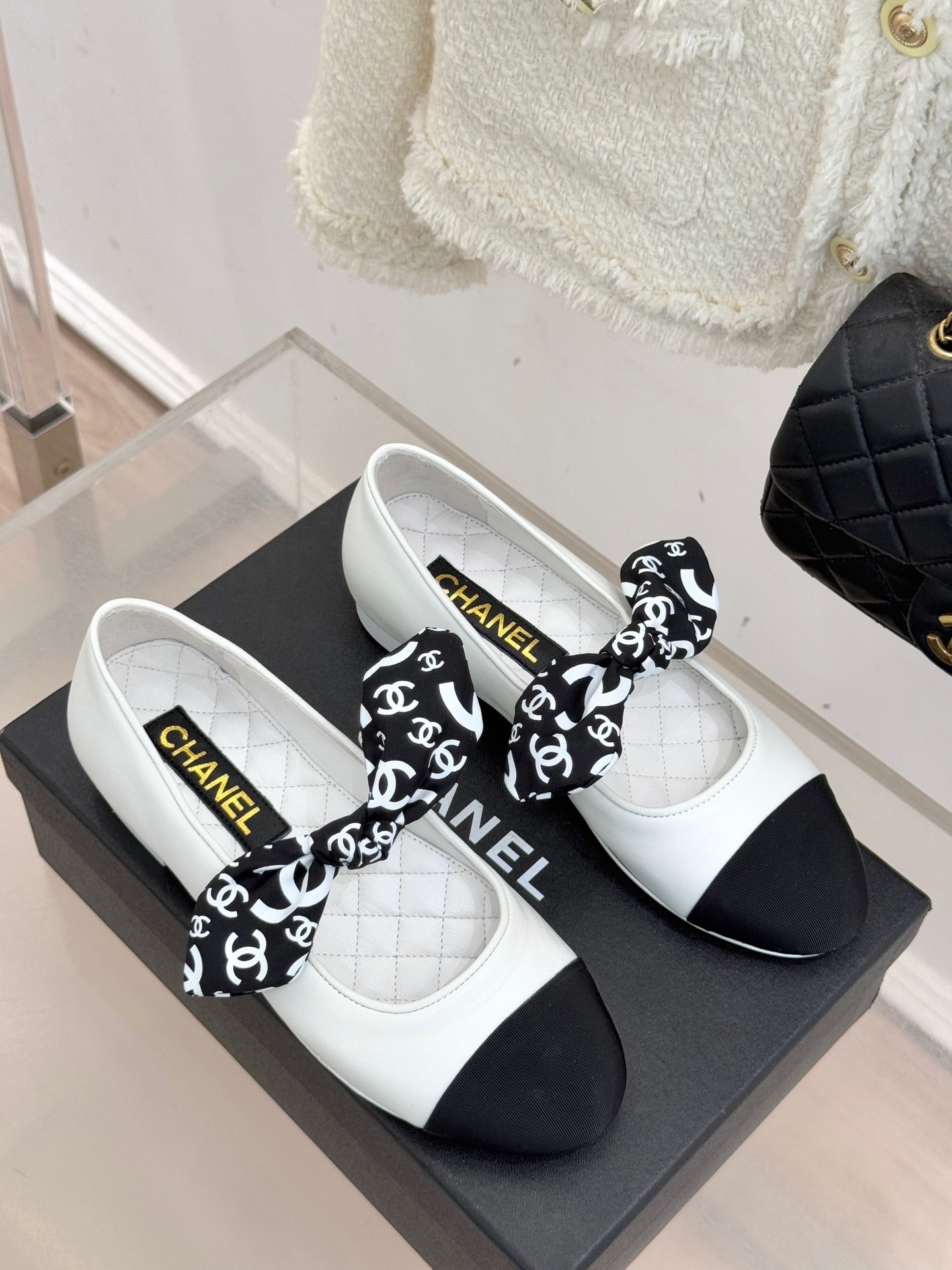 Pair of white Chanel ballet flats with black toe caps and black patterned bow.