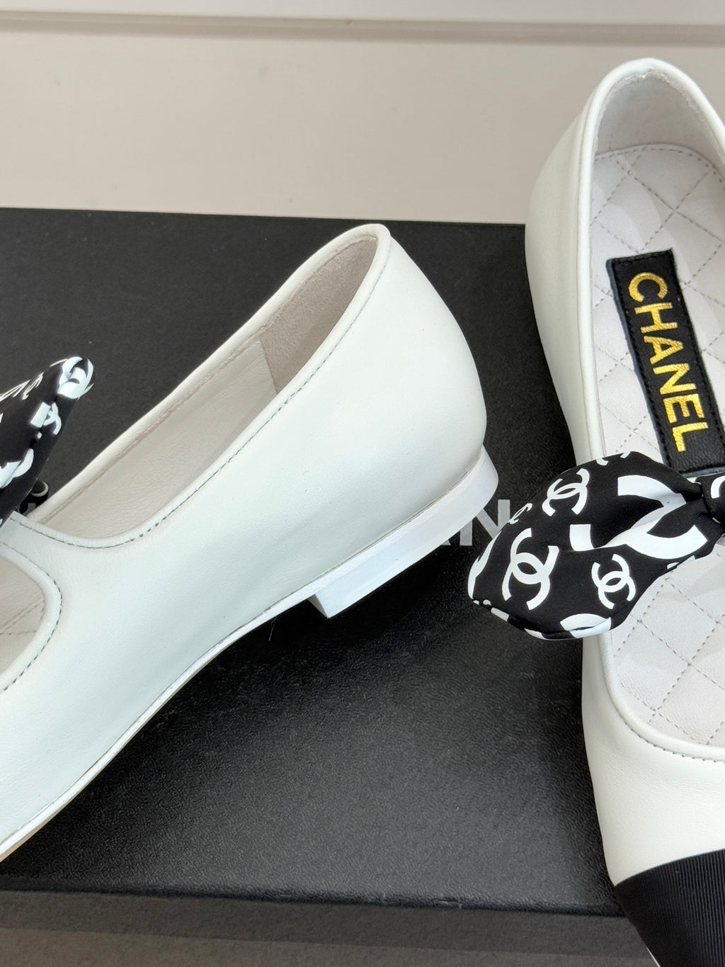 Close-up of white Chanel ballet flats on box with black patterned bow.