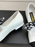 Close-up of white Chanel ballet flats on box with black patterned bow.