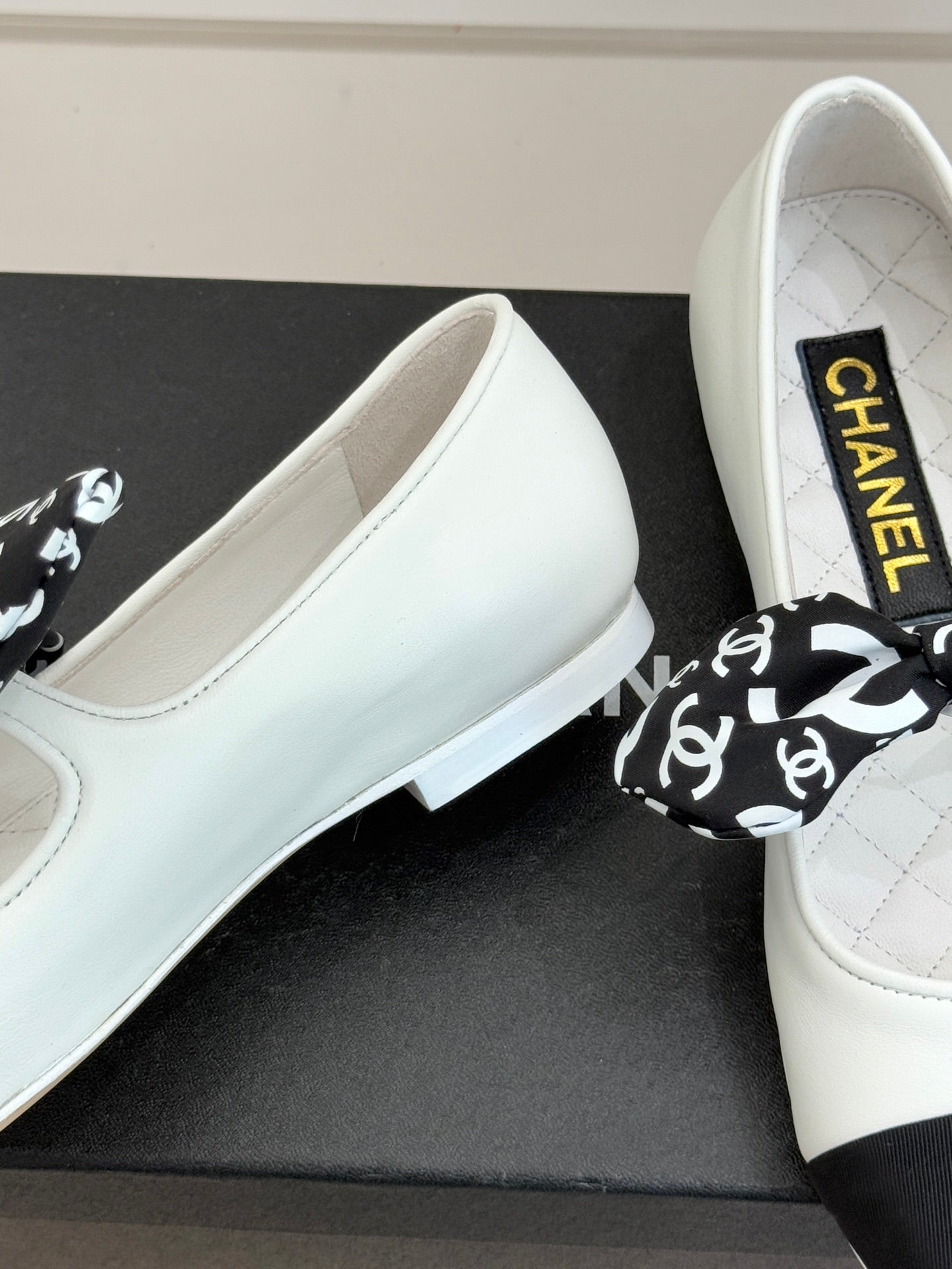 Close-up of white Chanel ballet flats on box with black patterned bow.