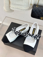 White Chanel ballet flats with black toe, black patterned bow, and gold trim.