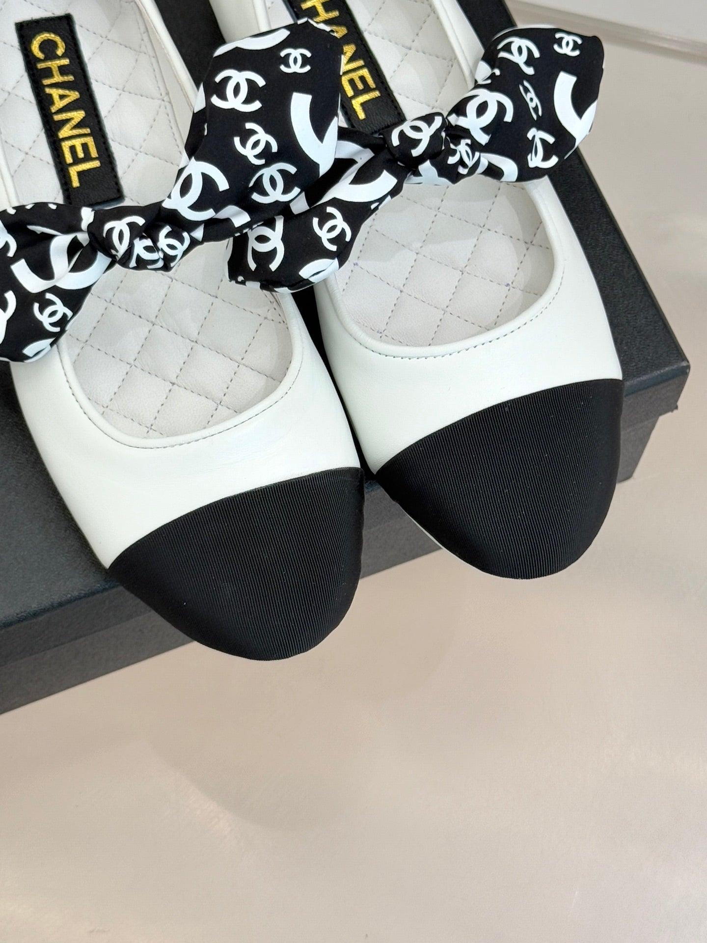 Chanel ballet flats in white with black toe and bow with CHANEL logo print.
