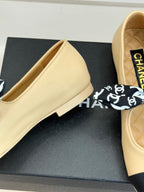 Beige flats close-up with navy sole edge; black logo bow detail on upper